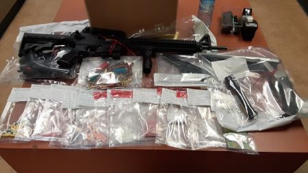 Weapons and evidence bags featuring firearm ammunition and suspected illegal guns, are displayed on a table. 