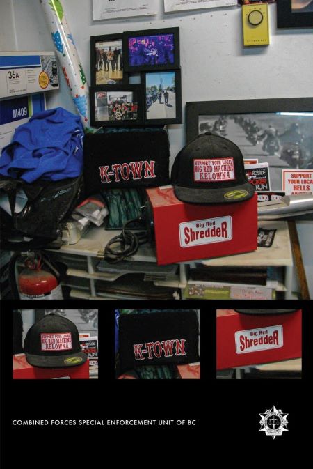 Items: A photo of items seized, including black caps with red letters K-Town, Support Your Local Big Red Machine Kelowna, and a red box with the words Big Red Shredder. The items sit on a shelving unit. A black and white photo of people on motorcycles is on a wall behind them. The words Combine Forces Special Enforcement Unit of BC and a logo are written in small write letters on the bottom of the image.