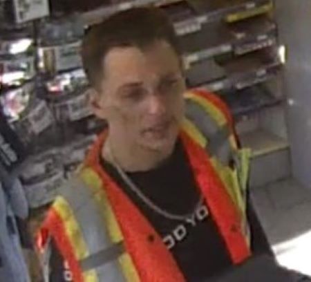 A man with shorter dark hair and bruises or markings on his face, wearing a high vis vest with a necklace and black chain underneath it. 