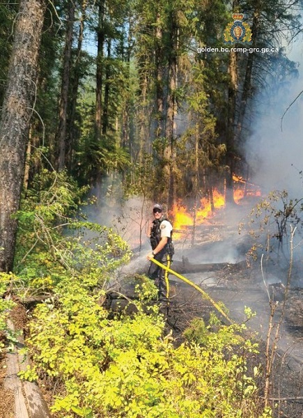 Photo of Constable Mark Tataryn standing in a forest holding a hose and spraying water on visible flames in the background