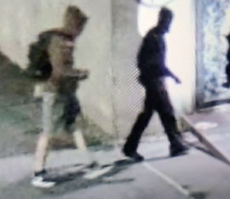 Suspects à l’extérieur : un suspect vêtu d’un chandail à capuchon brun ou vert et d’un short portant un sac à dos à côté d’une personne vêtue de vêtements foncés, marchant à l’extérieur.
