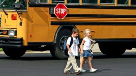 Autobus scolaire : deux jeunes enfants portant des sacs à dos marchent devant un autobus scolaire
