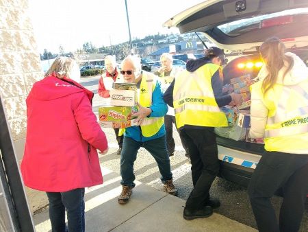  Volunteers in yellow reflective vests accept an armload of donated toys from a woman in a red coat, and load them into the back of a police SUV.