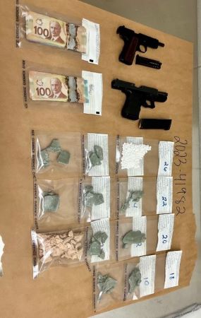 Armes à feu, drogues emballées et argent sont exposés sur une table.
