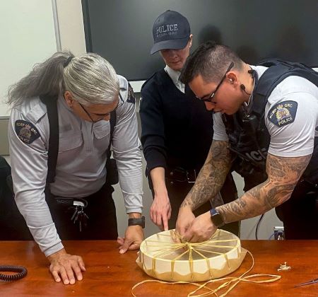 Three police officers work on a traditional circular hand drum on a table in front of them. 